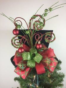 a christmas tree with ornaments on it and a bow hanging from the top, in front of a white wall