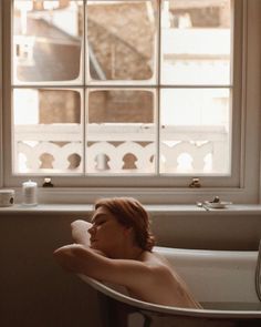 a woman laying in a bathtub next to a window