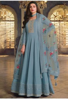 a woman standing in a blue dress with floral embroidery on the sleeves and bottom, wearing a