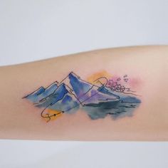 a watercolor tattoo on the arm of a woman with mountains and flowers in the background