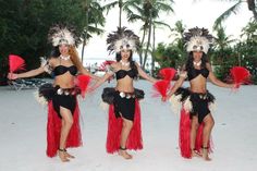 three beautiful women in red and black costumes standing on the beach with palm trees behind them