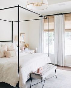 a white bedroom with four poster bed and curtains on the window sill above it