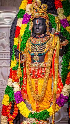 a statue of the hindu god person in front of a flowered wall with flowers around it