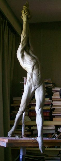 a sculpture of a man standing on top of a table next to stacks of books