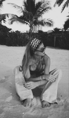 a black and white photo of a woman sitting on the beach with palm trees in the background