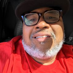 a man wearing glasses and a hat in the back seat of a car with his tongue out