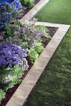 a garden with green grass and purple flowers in the center, next to a sidewalk