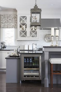 a kitchen with white cabinets and gray counter tops, an island in the middle has a wine cooler on it