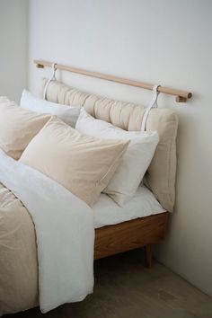 an unmade bed with white sheets and beige pillows in a small room next to a window