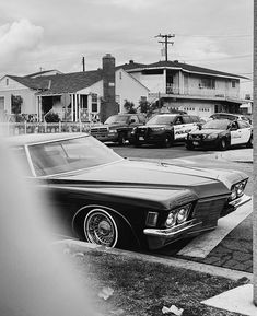 black and white photograph of an old car parked on the side of the road in front of some houses