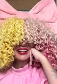 a woman with blonde and pink curly hair is laying on a bed wearing a pink bow