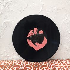 a black record with pink hand prints on the front and side, against a white wall