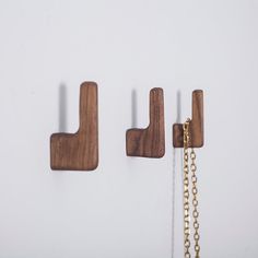 three wooden hooks hanging on the wall with chains attached to them and one has a gold chain in front of it