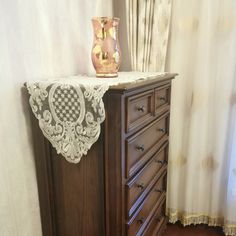 a dresser with a vase on top of it next to a curtained window sill