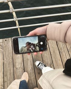 someone taking a photo with their cell phone while sitting on a dock next to the water