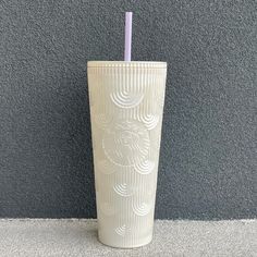 a white cup with a purple straw sticking out of it's side next to a gray wall