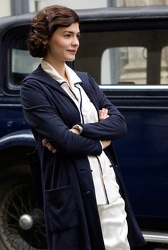 a woman standing in front of an old car with her arms crossed and looking at the camera