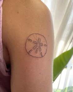 a small sand dollar tattoo on the back of a woman's left upper arm