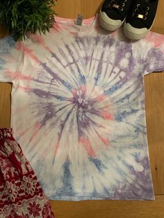 a tie - dyed shirt and pair of sneakers are on the floor next to a potted plant