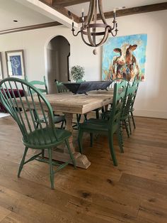 a dining room table with green chairs and a cow painting on the wall behind it