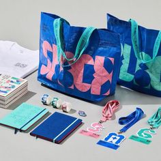 two blue bags with pink and green designs on them next to some other items that include books