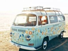 an old vw bus with flowers painted on the side parked in front of water