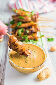 a person dipping something into a small bowl with skewers on the side next to them