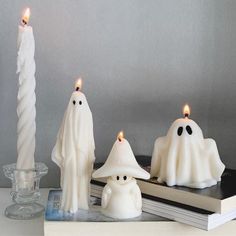 three candles with ghost faces on them sitting next to a stack of books and a candle holder