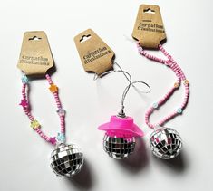 three disco ball ornaments with pink ribbon and tags attached to each ornament on a white surface