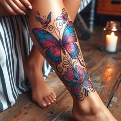 a woman's legs with butterfly tattoos on them, sitting next to a candle