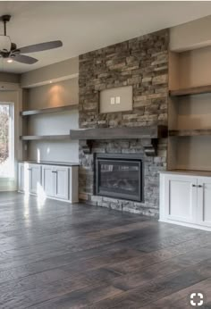 an empty living room with stone fireplace and built - in shelving