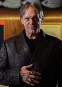 a man in a leather jacket standing next to a wall with pictures on the walls