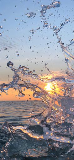 the sun is setting over the ocean with water splashing on it's surface