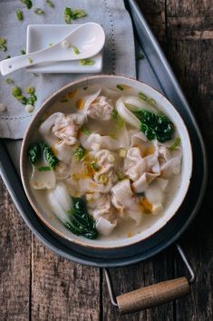 a bowl filled with dumplings and vegetables on top of a wooden table next to a spoon