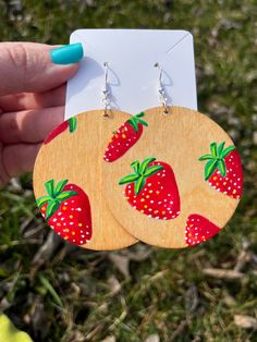 a pair of earrings with strawberries painted on them are being held by a person