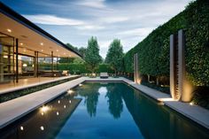 an outdoor swimming pool surrounded by greenery and lights at dusk with modern architecture in the background