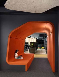 a woman sitting on an orange bench in the middle of a room with black walls