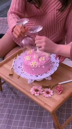 a woman is decorating a pink cake on a tray with flowers and spoons