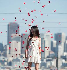 a woman standing on top of a hill surrounded by red petals in front of a city skyline