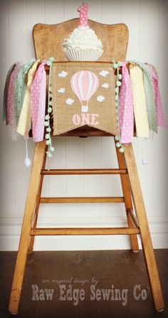 a wooden high chair with a cupcake on the top and some ribbons around it