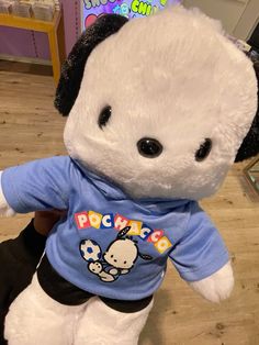 a white stuffed bear with a blue shirt on it's chest and black ears