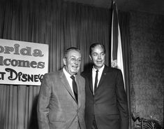 two men standing next to each other in front of a sign that says florida welcomes direct disney