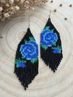 blue and black seed beaded earrings sitting on top of a piece of wood next to dried flowers