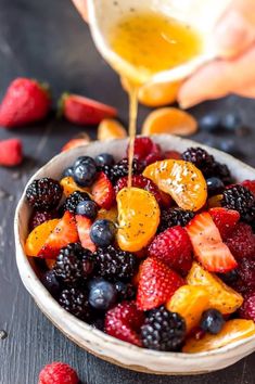 someone pouring orange juice into a bowl of mixed berries and raspberries for a fruit salad