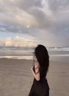 a woman standing on top of a sandy beach next to the ocean under a cloudy sky