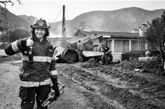 black and white photograph of fireman in front of destroyed house with firefighters nearby on dirt road