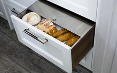 an open drawer in a kitchen filled with breads and pastries on the counter