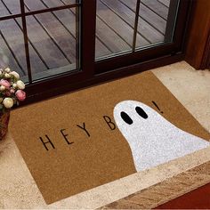 a door mat that says hey boo with a ghost face on it next to a potted plant