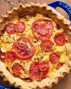 a pie with tomatoes and herbs in it on a blue plate next to a fork