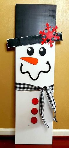 a snowman made out of construction paper on the side of a wall with a black and white checkered ribbon